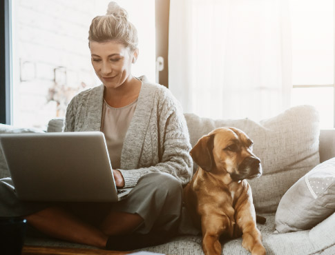 a woman working on her laptop while sitting next to her dog